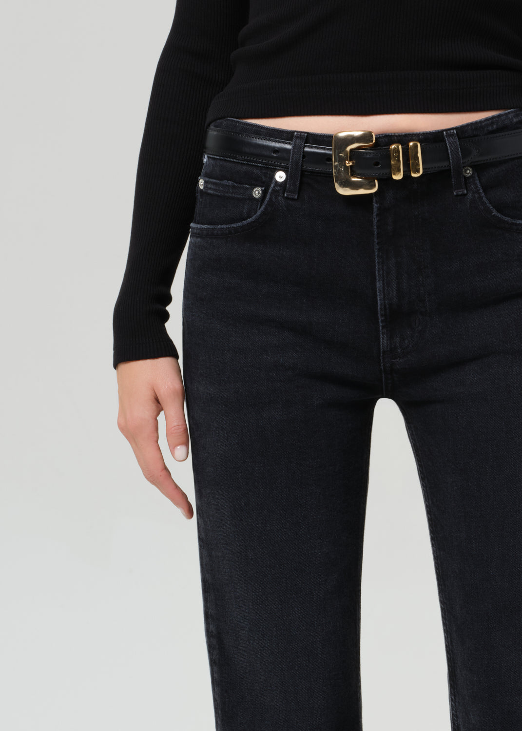 Black jeans with a gold belt buckle on a gray background