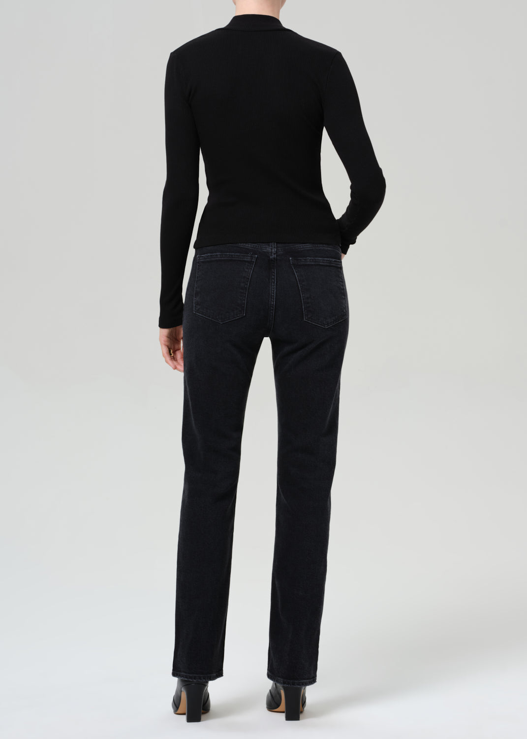 Person wearing a black sweater and black jeans on a plain background