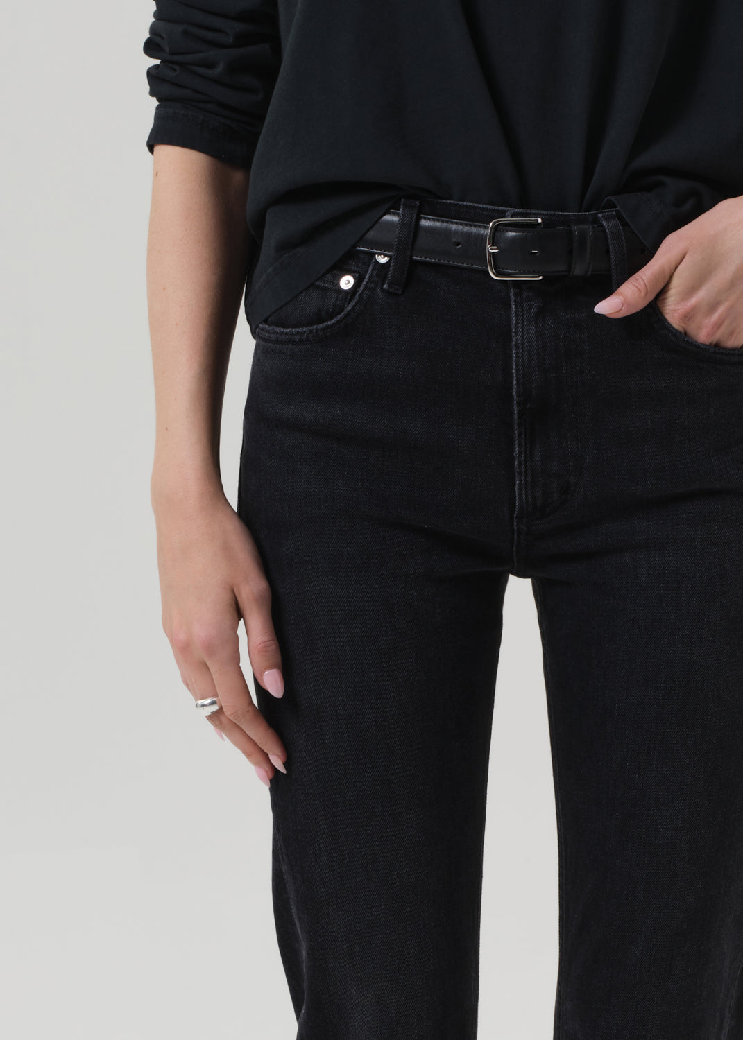 Person wearing a black outfit with a turtleneck and jeans on a grey background