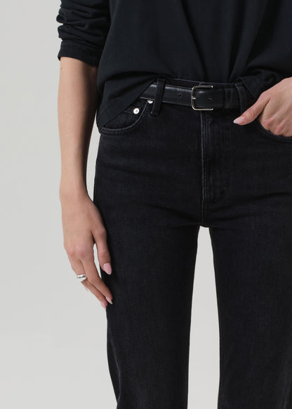 Person wearing a black outfit with a turtleneck and jeans on a grey background