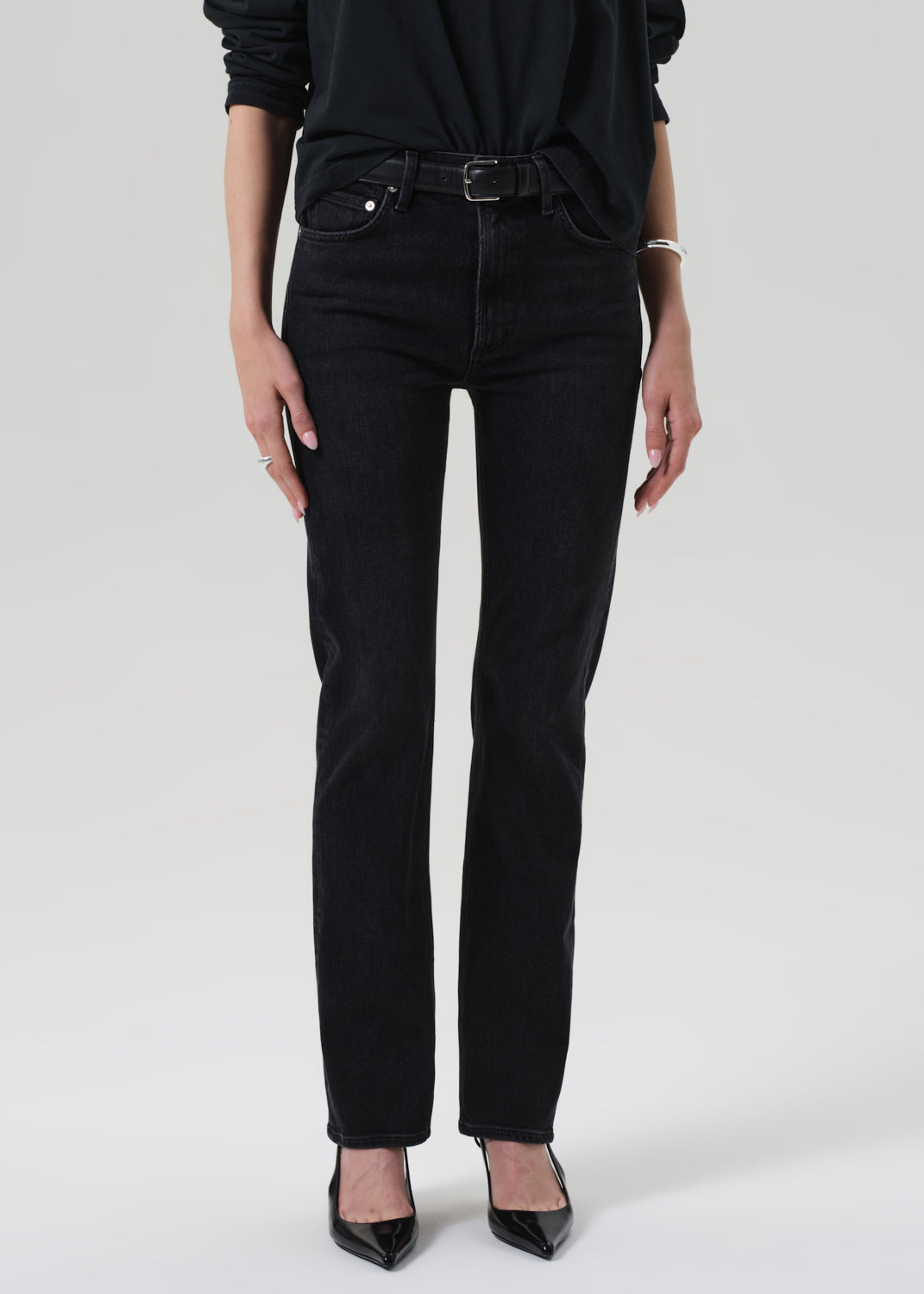 Person wearing a black outfit with a turtleneck and jeans on a grey background