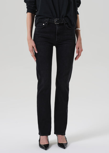 Person wearing a black outfit with a turtleneck and jeans on a grey background