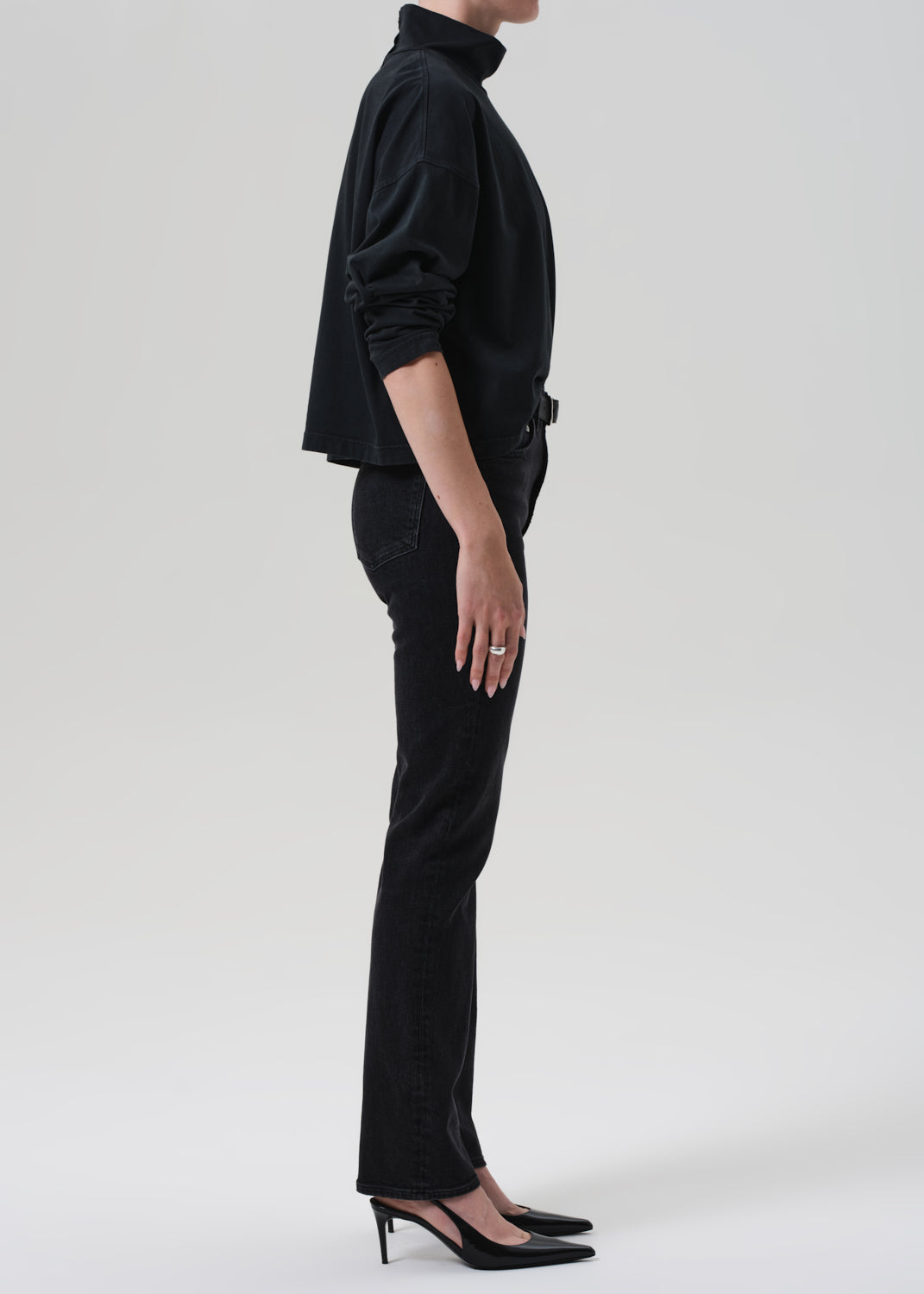 Person wearing a black outfit with a turtleneck and jeans on a grey background
