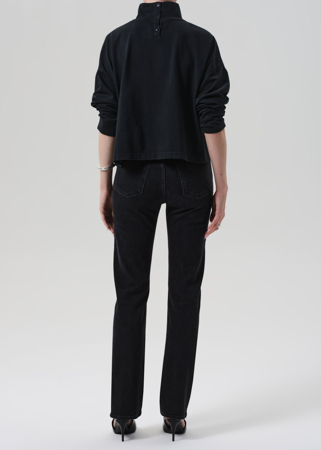 Person wearing a black outfit with a turtleneck and jeans on a grey background