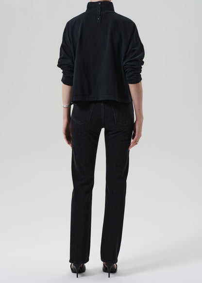 Person wearing a black outfit with a turtleneck and jeans on a grey background