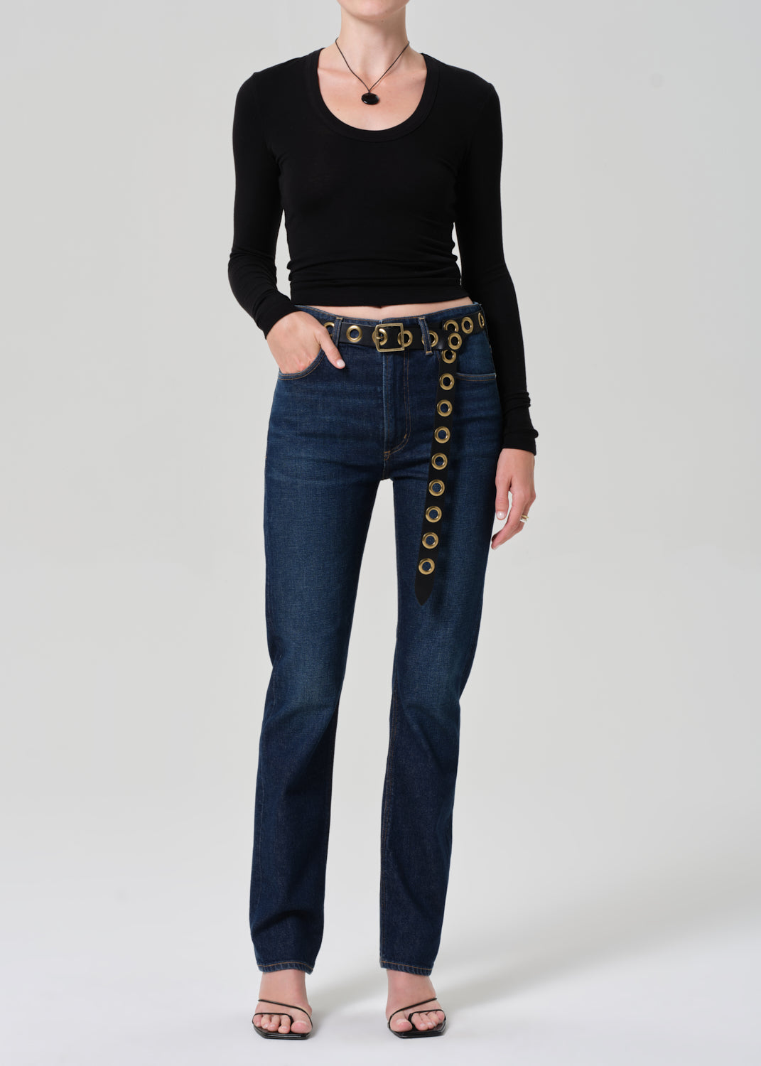 Person wearing blue jeans with decorative buttons and a black top on a  plain background