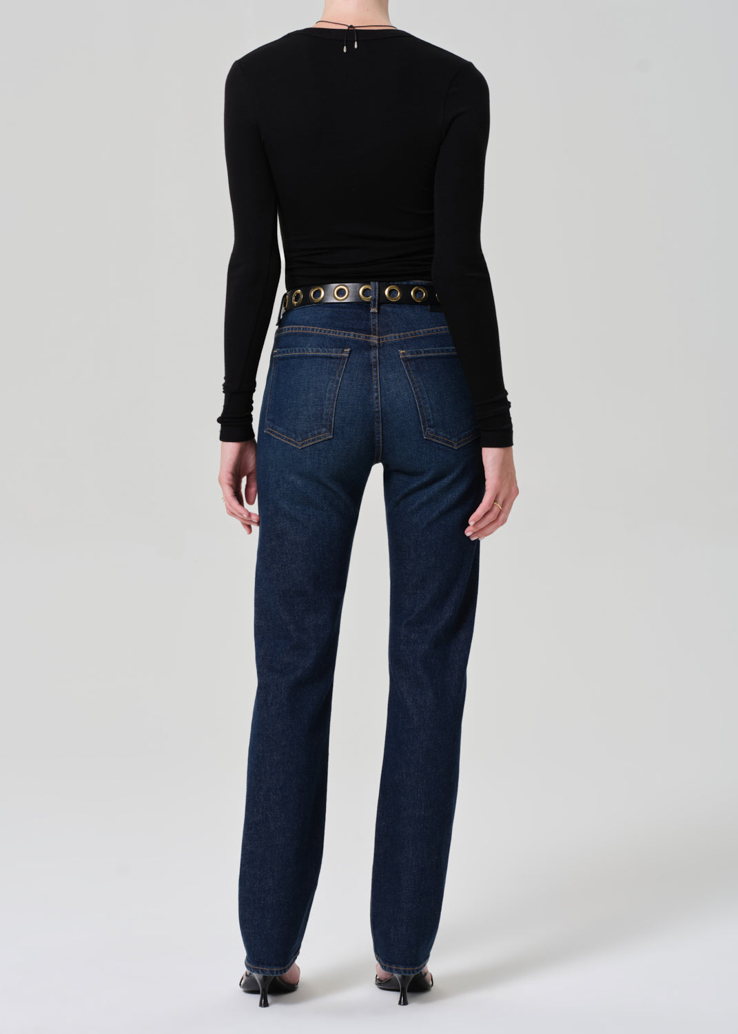 Person wearing a black long-sleeve top and blue jeans on a white background