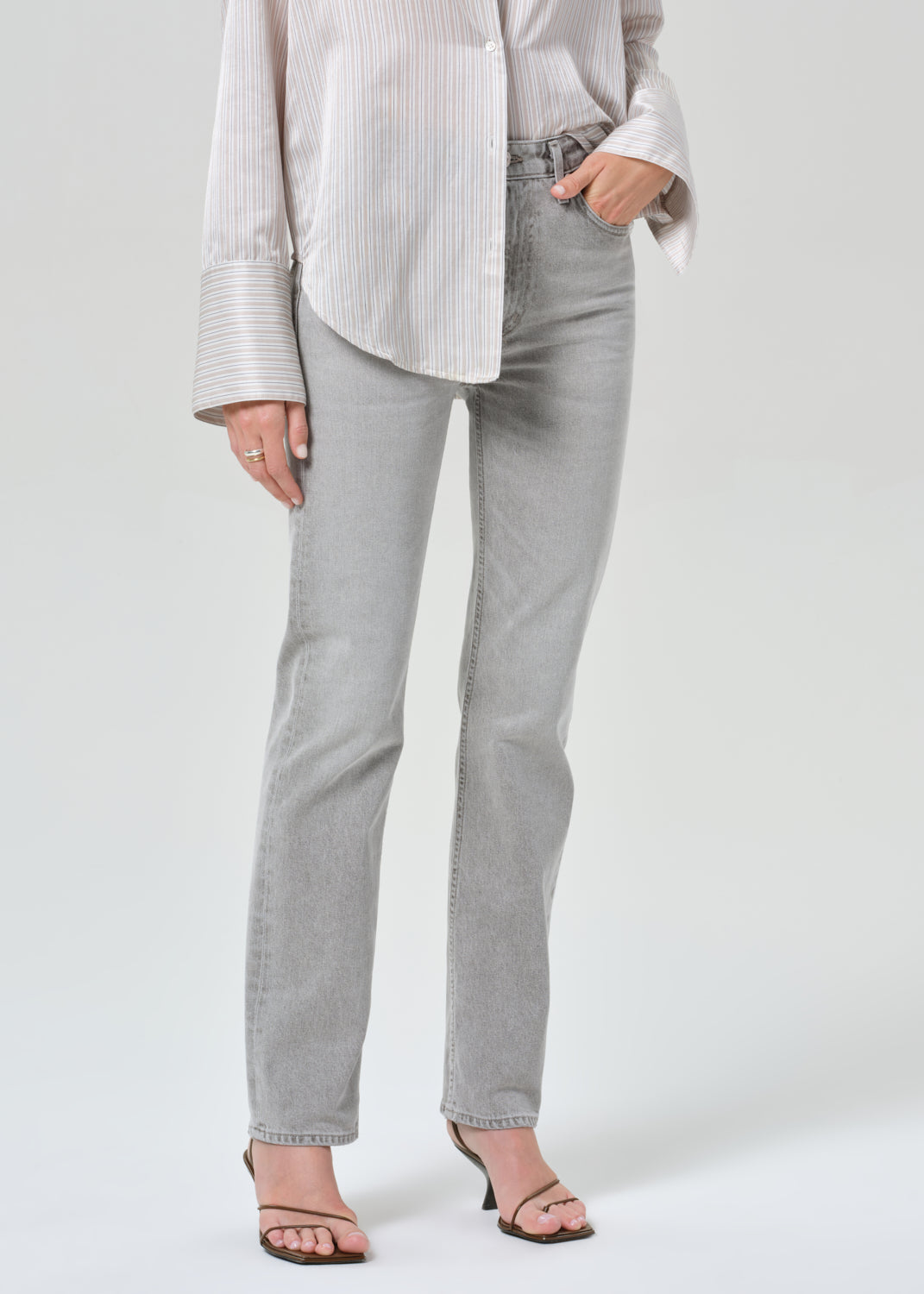 Person wearing a light gray stripe shirt and jeans on a grey background