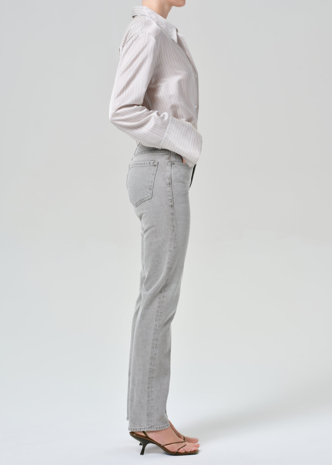 Person wearing a light gray stripe shirt and jeans on a grey background