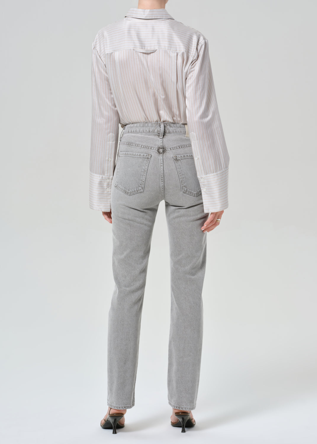 Person wearing a light gray stripe shirt and jeans on a grey background