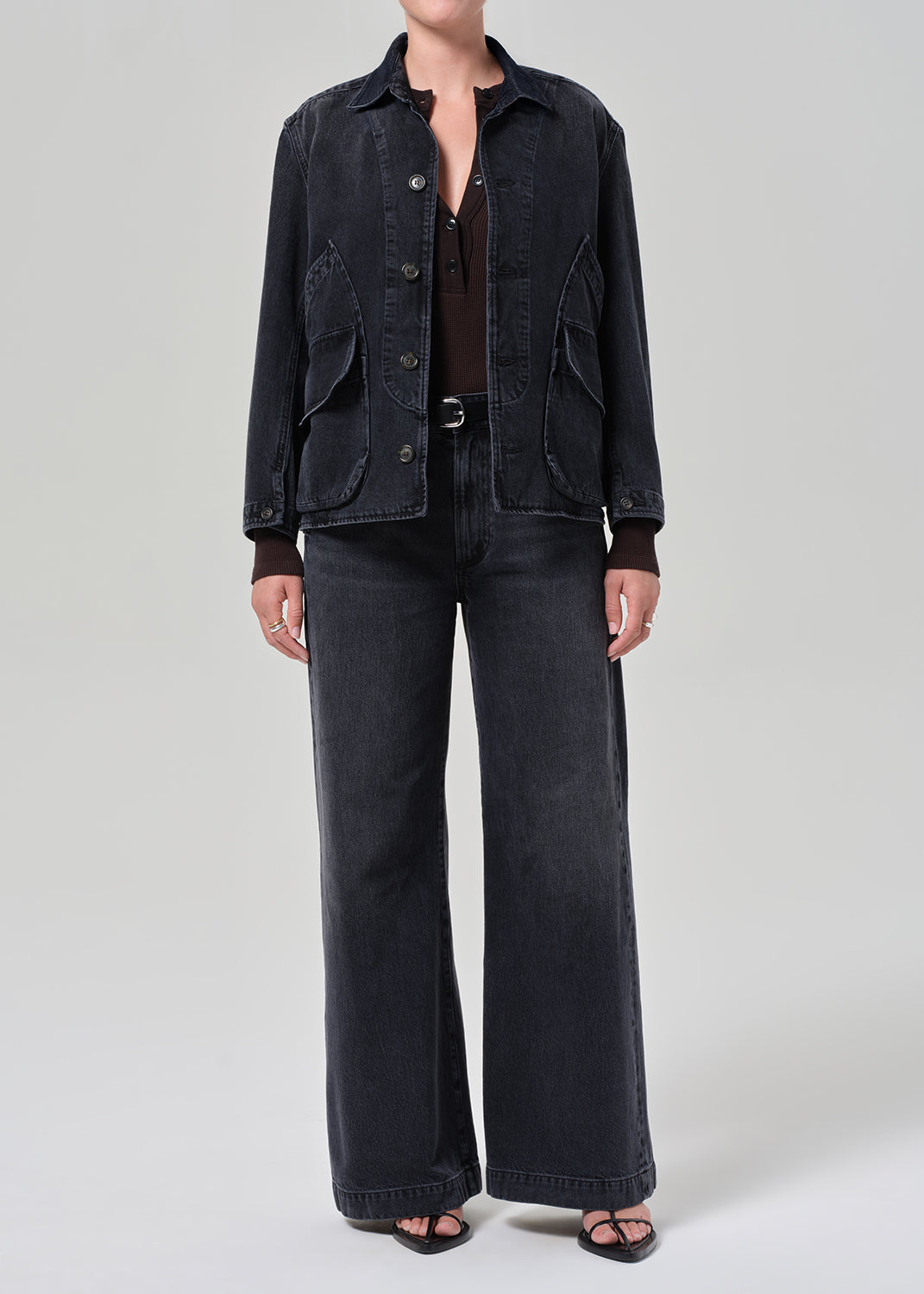 Person wearing a black denim jacket and wide-leg jeans on a plain background