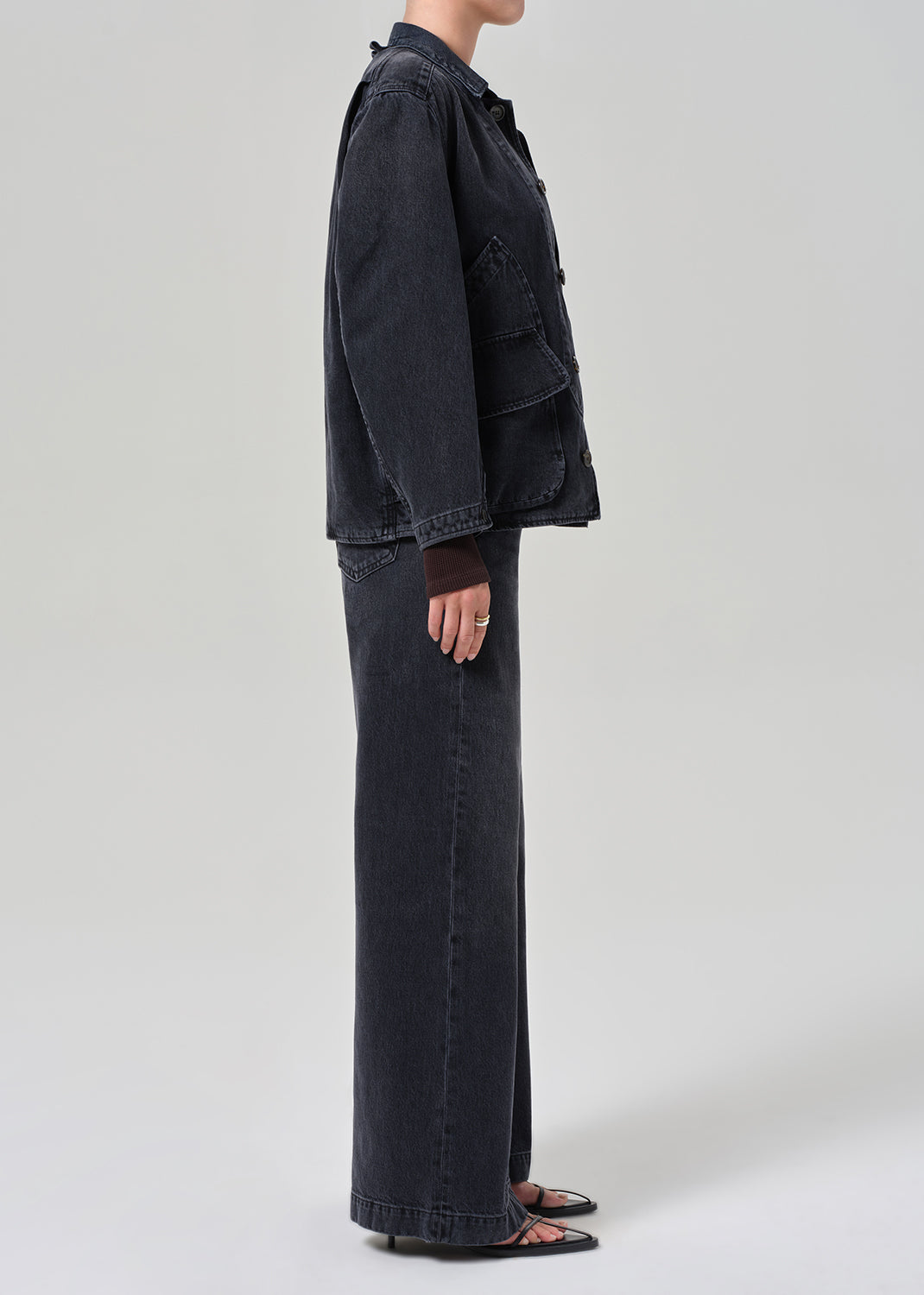 Person wearing a dark denim jacket and wide-leg jeans on a light gray background