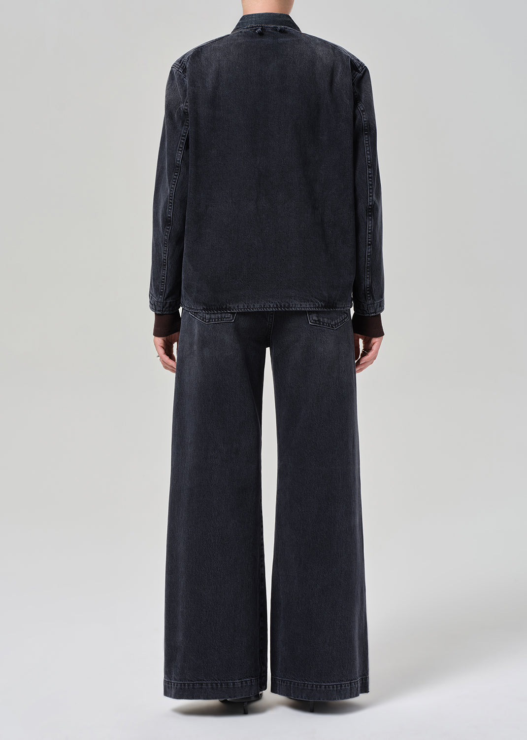 Person wearing a dark denim jacket and wide-leg jeans on a light gray background