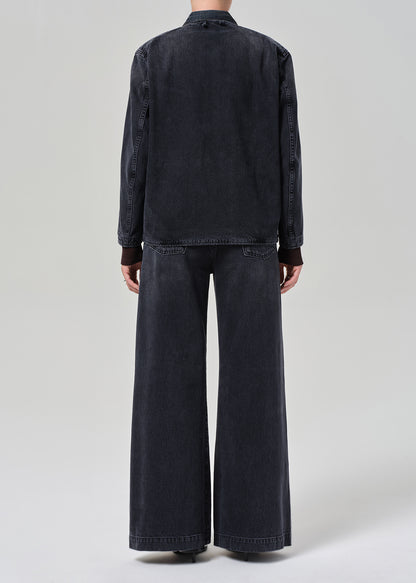 Person wearing a dark denim jacket and wide-leg jeans on a light gray background