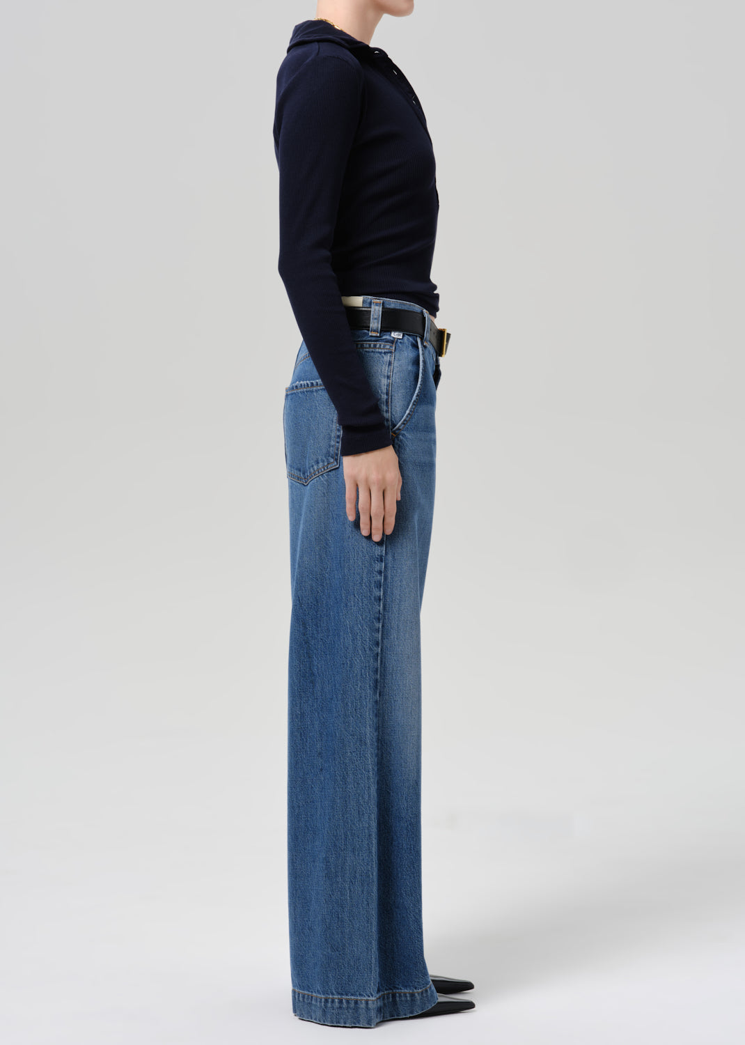 Person wearing a dark sweater and blue pants on a grey background