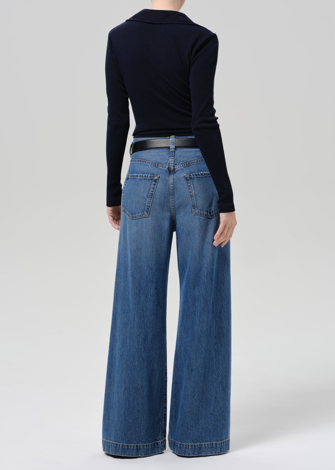 Person wearing a dark sweater and blue pants on a grey background