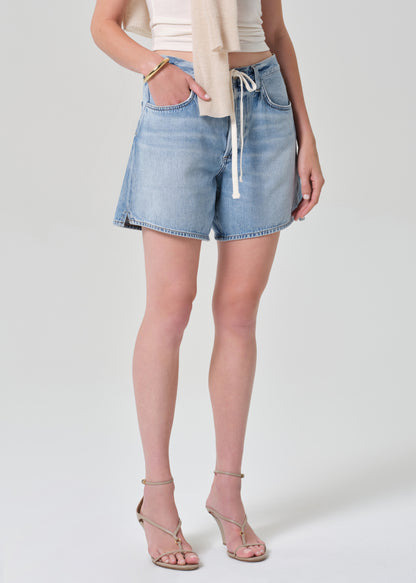 Person wearing light blue denim shorts on a grey background