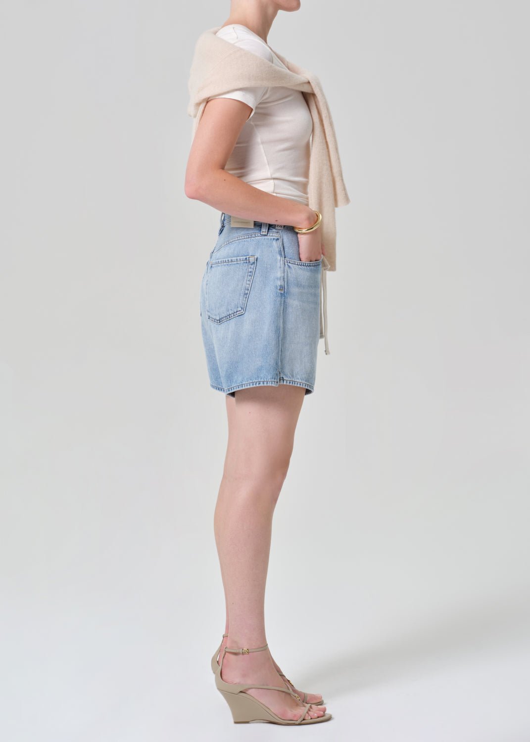 Person wearing a white top, light blue denim skirt, beige sweater, and beige sandals on a grey background