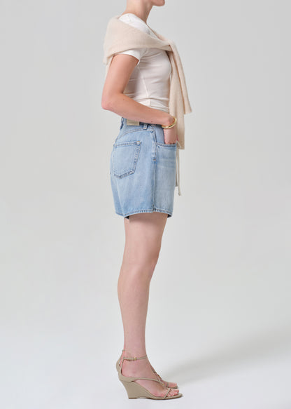 Person wearing a white top, light blue denim skirt, beige sweater, and beige sandals on a grey background
