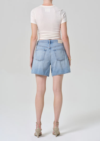 Person wearing light blue denim shorts and a white top on a plain background
