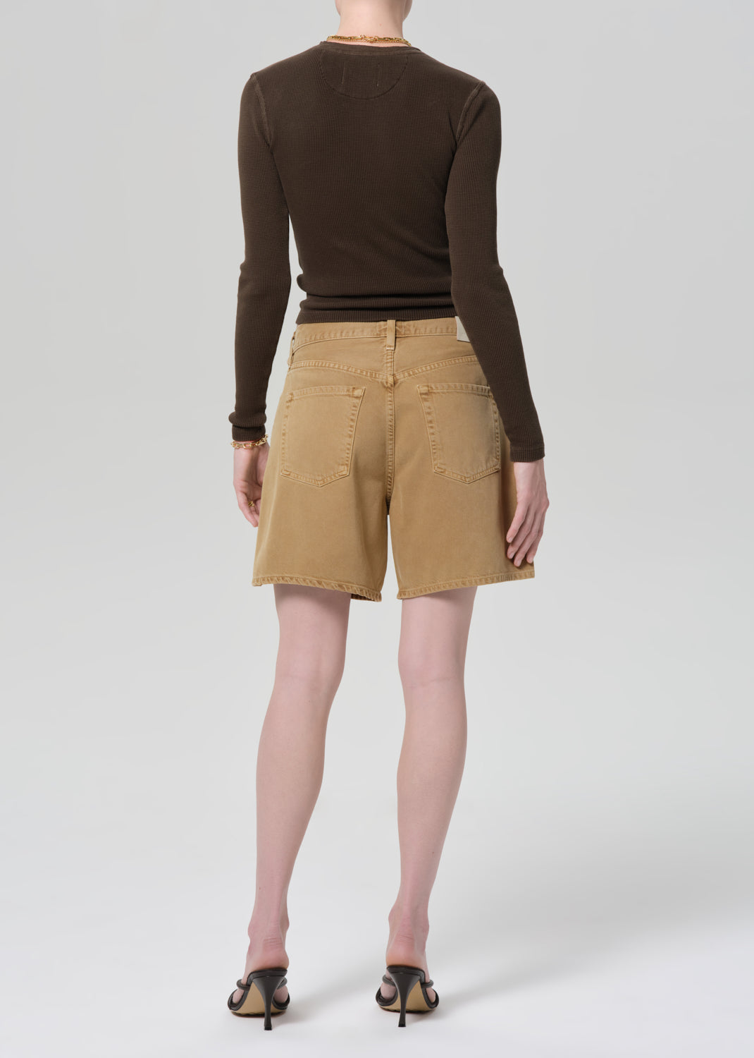 Person wearing a brown long-sleeve shirt and tan shorts on a plain background
