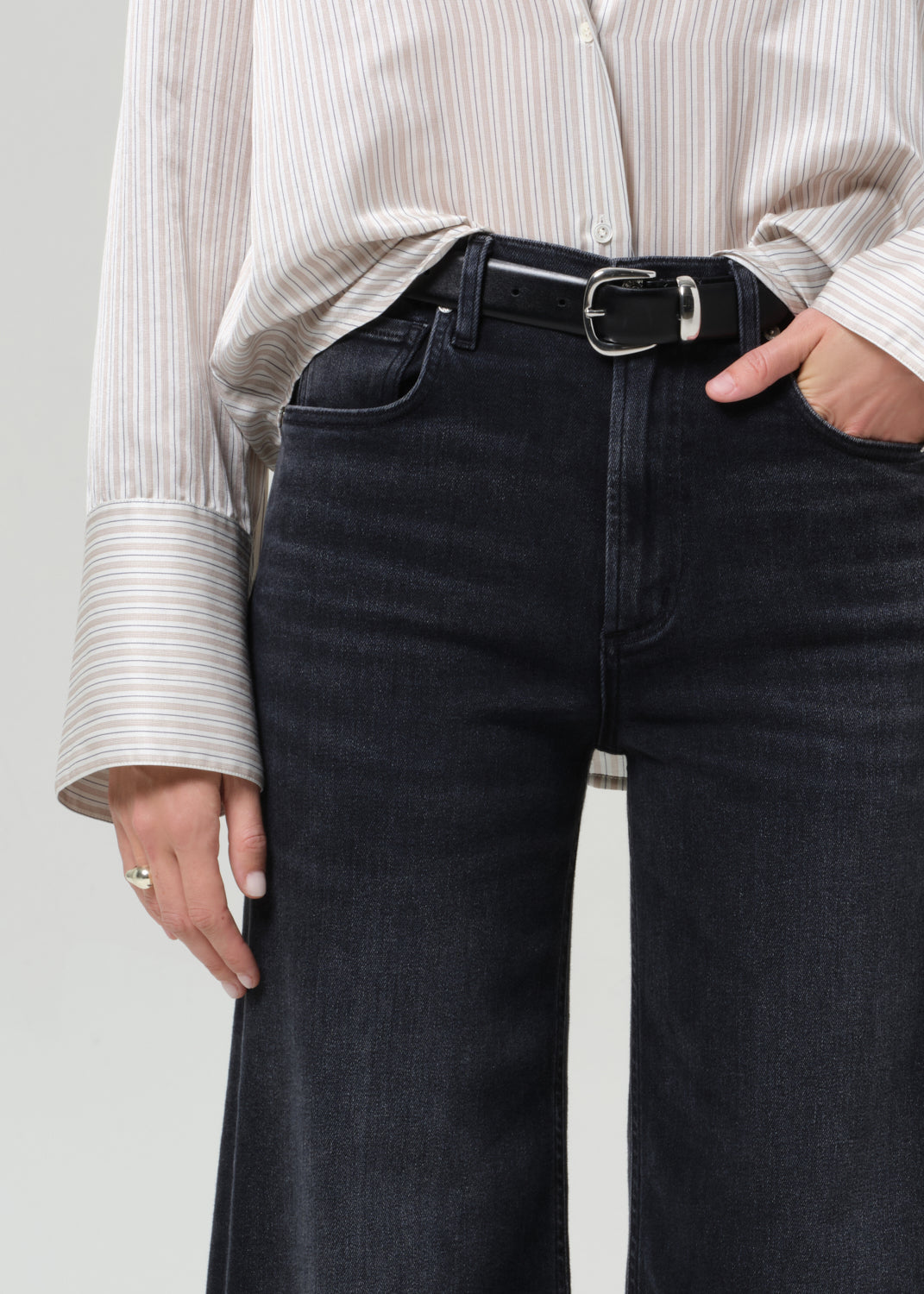 Person wearing black jeans and a light-colored shirt against a neutral background