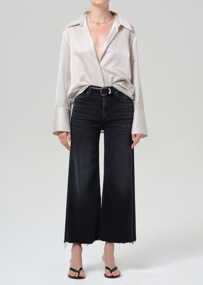 Person wearing a light-colored button-up shirt and black wide-leg pants on a plain background