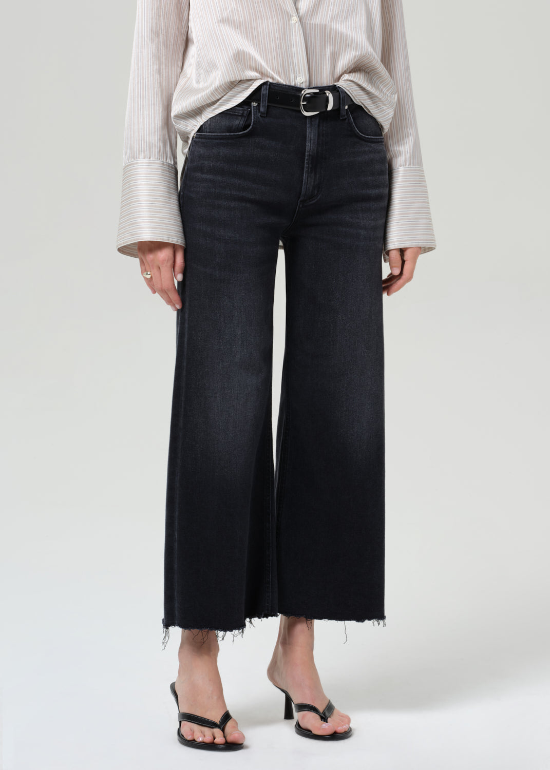 Person wearing black wide-leg jeans and a light-colored shirt on a grey background