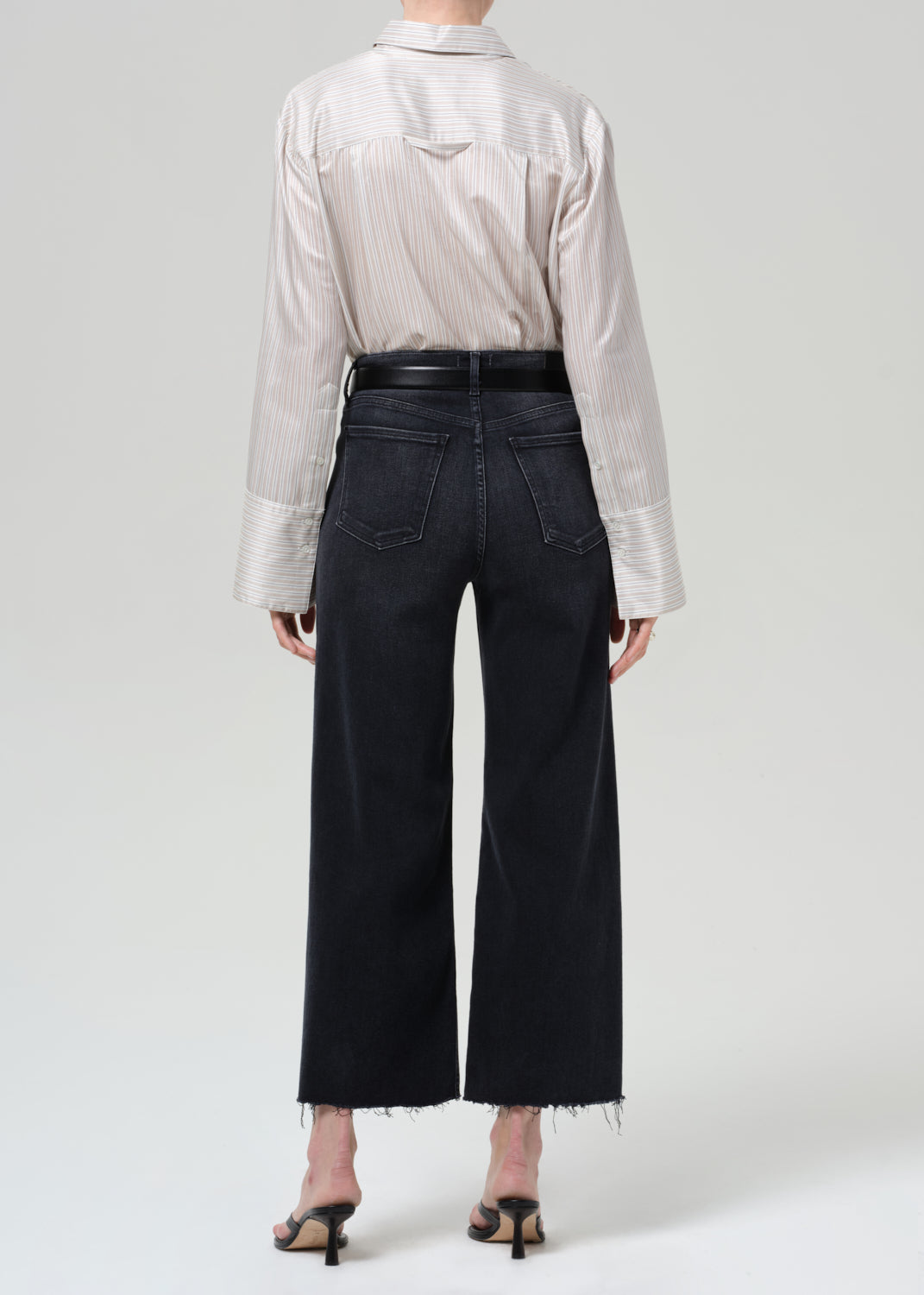 Person wearing a light-colored shirt and black wide-leg jeans on a plain background