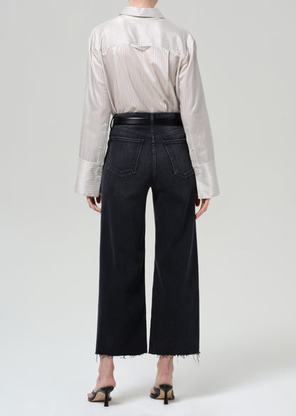 Person wearing a light-colored shirt and black wide-leg jeans on a plain background