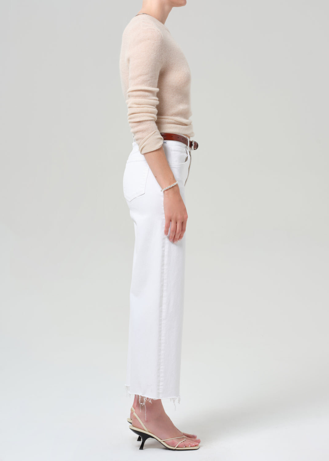 Person wearing a beige sweater and white pants on a plain background