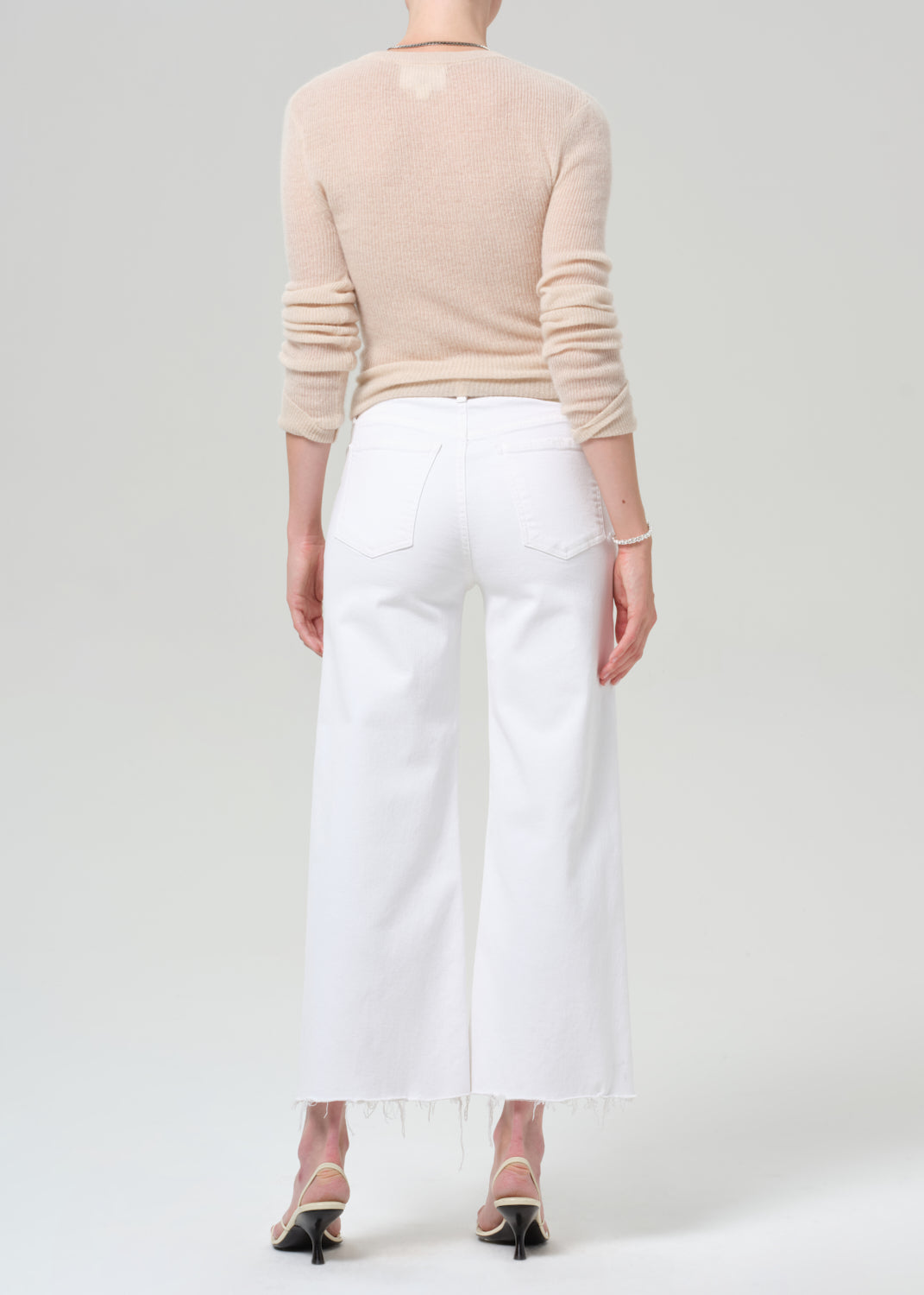 Person wearing a beige long-sleeve top and white pants on a plain background