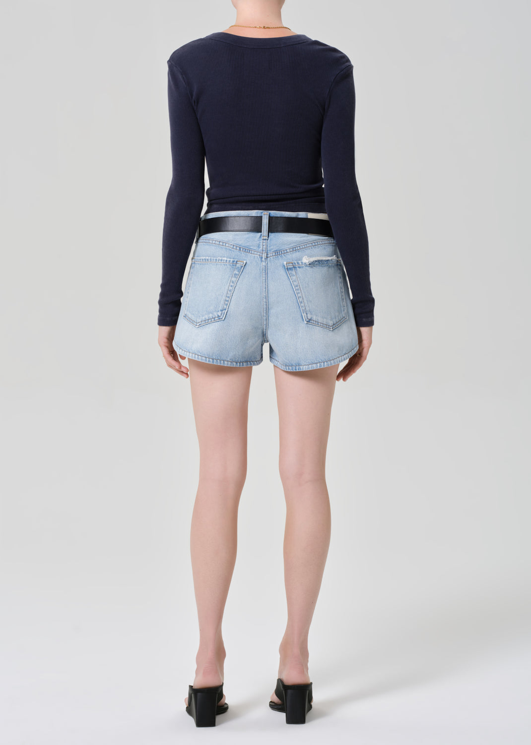 Person wearing a navy long-sleeve top and light blue denim shorts on a grey background