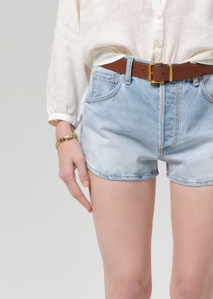 Person wearing light blue denim shorts with a brown belt on a plain background