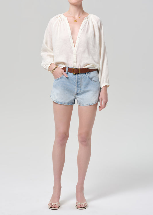 Person wearing a white blouse and light blue denim shorts on a plain background