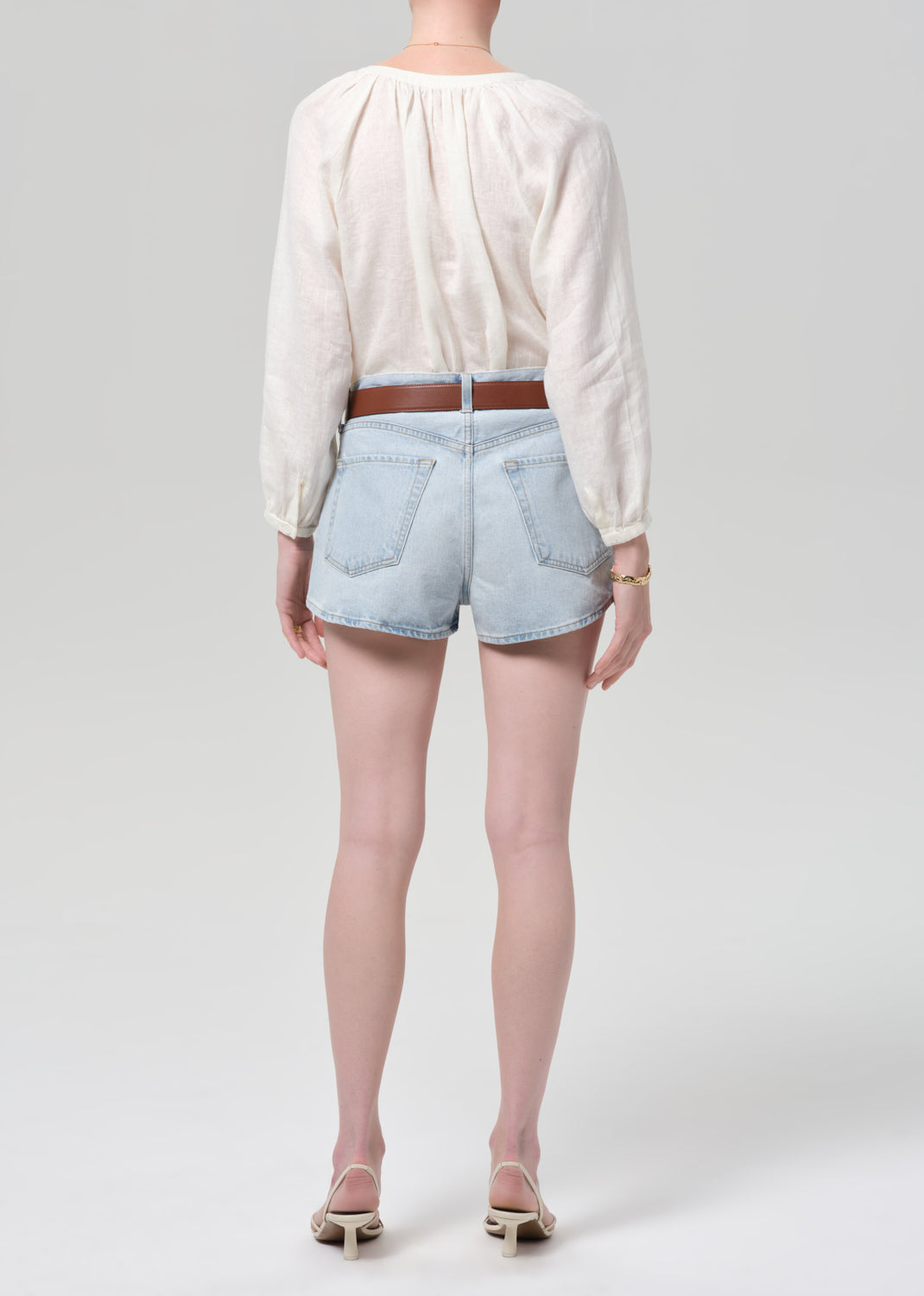 Person wearing a white blouse and light blue denim shorts on a plain background