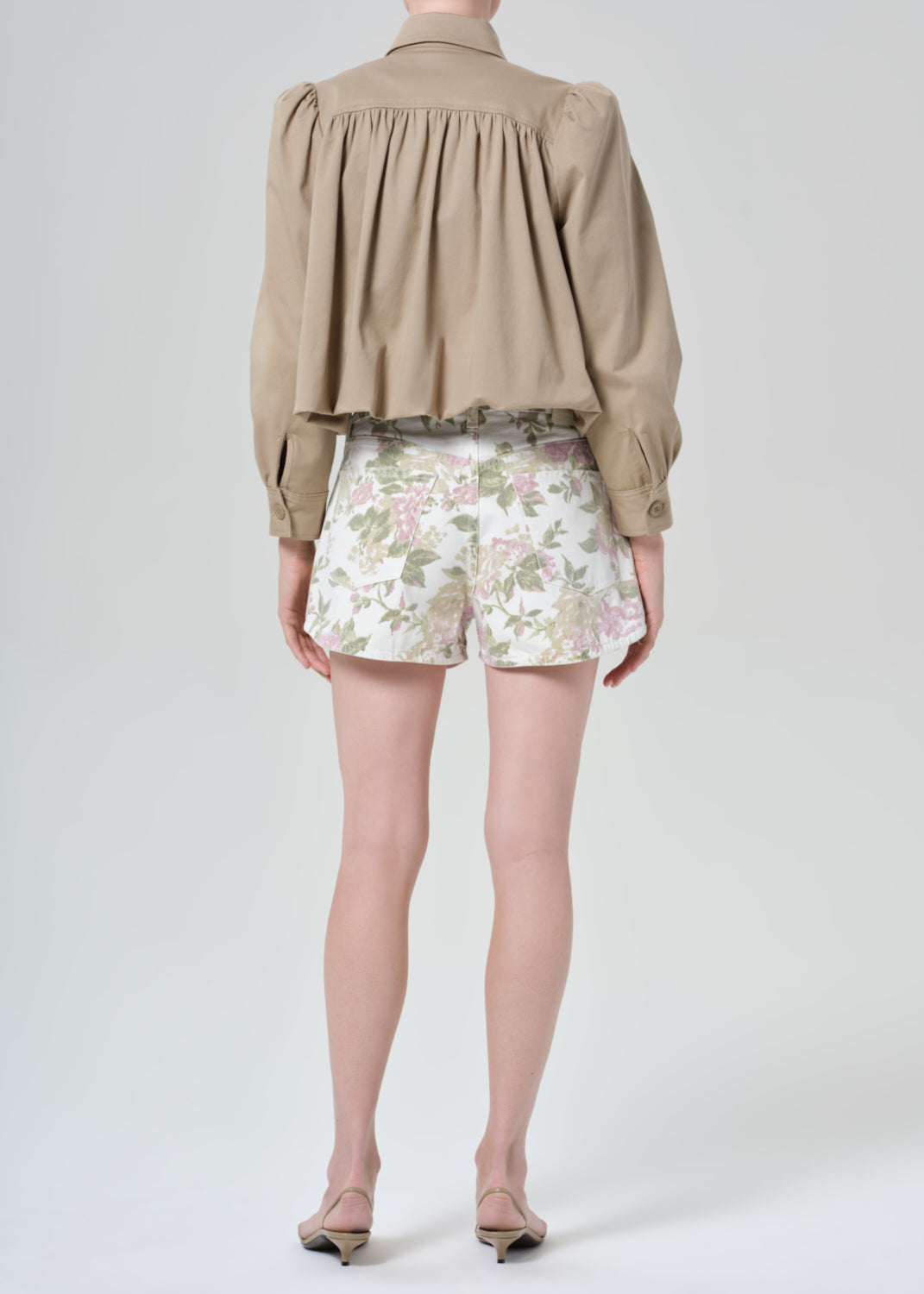 Person wearing a beige jacket and floral  denim shorts on a grey background