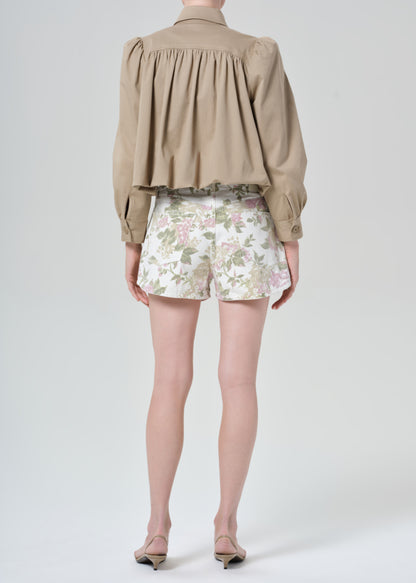 Person wearing a beige jacket and floral  denim shorts on a grey background