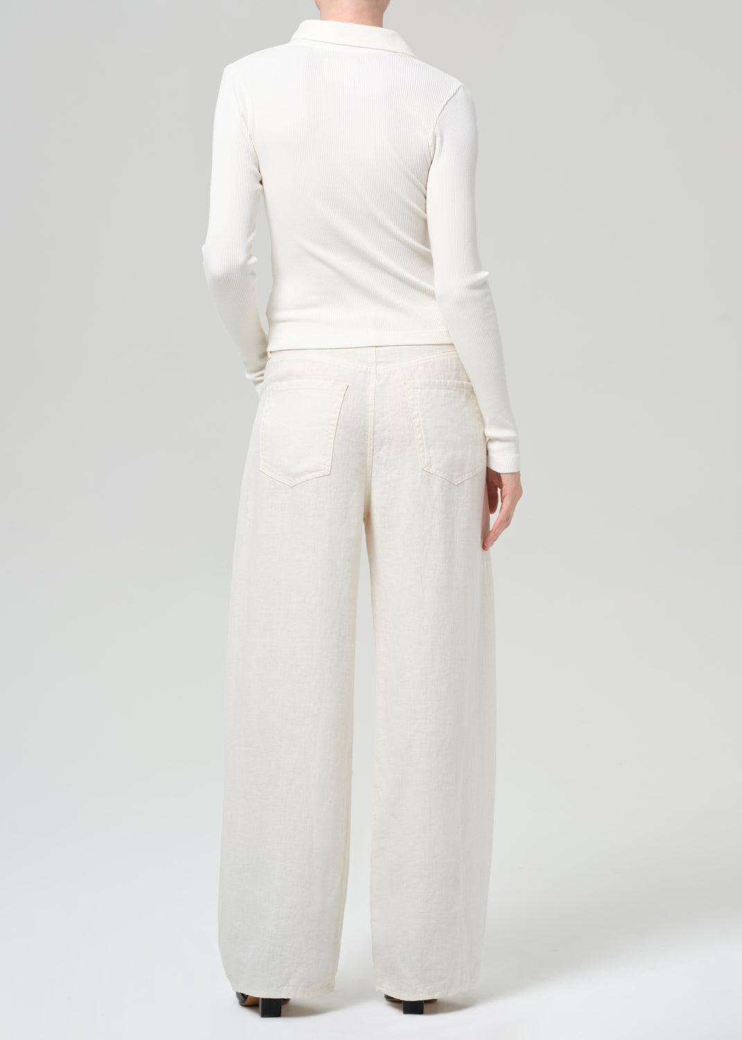 Person wearing a white outfit with wide-leg pants on a light gray background