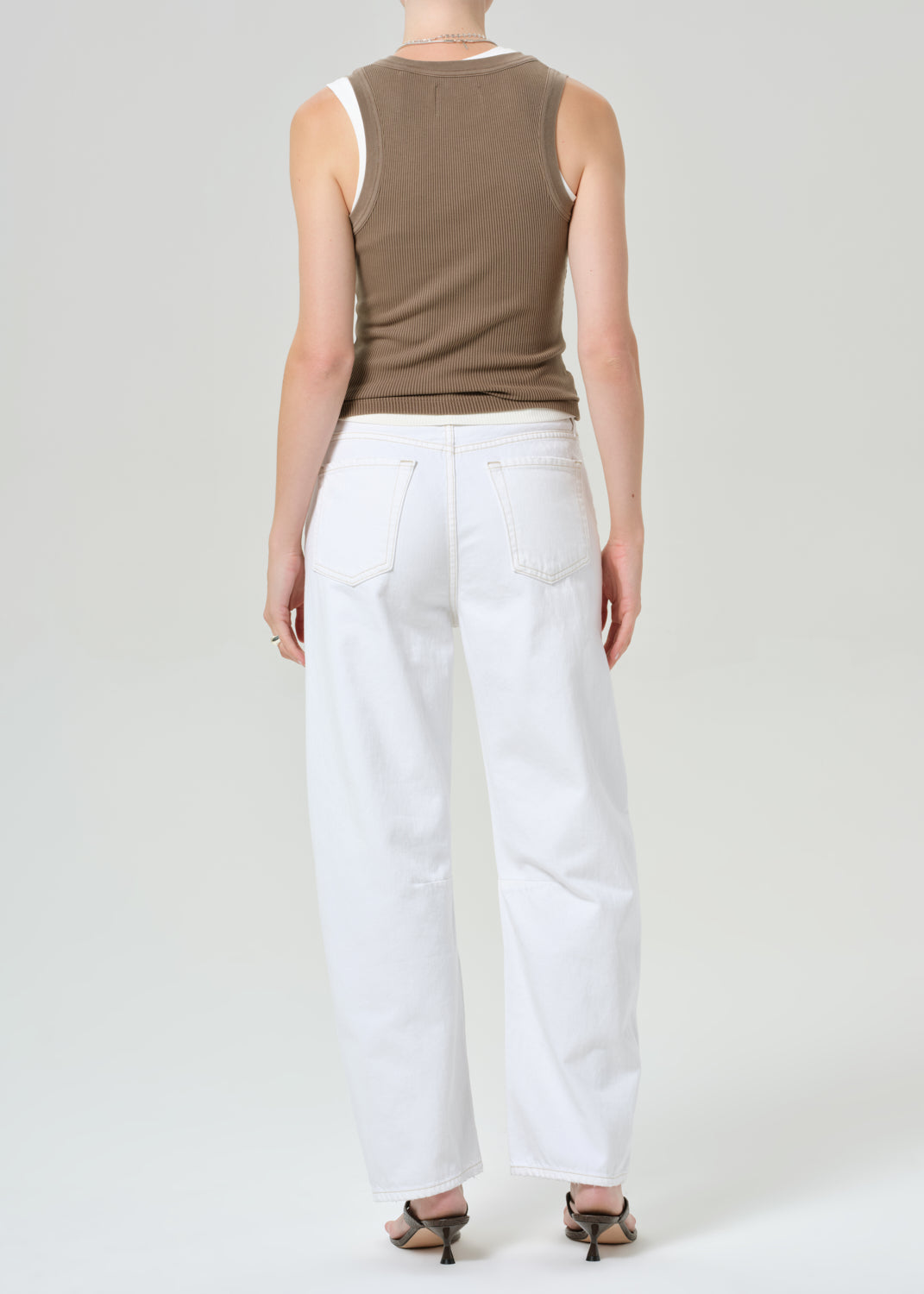 Person wearing a brown sleeveless top and white jeans on a plain background