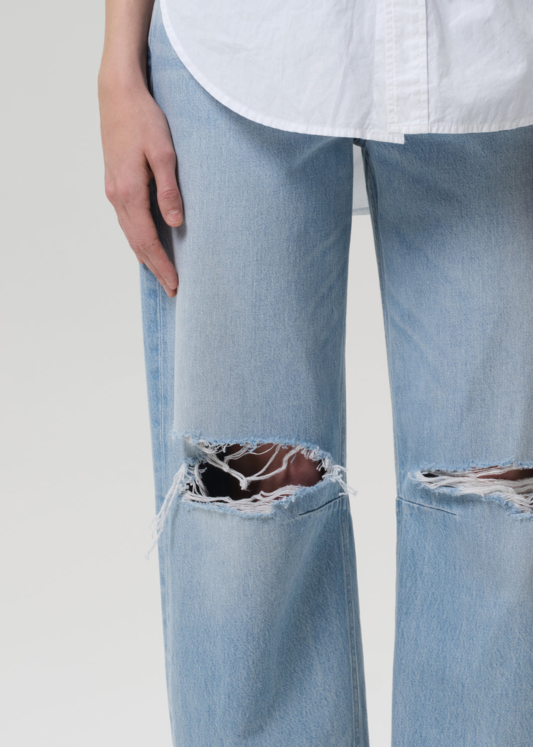 Light blue jeans with a ripped knee design on a plain background