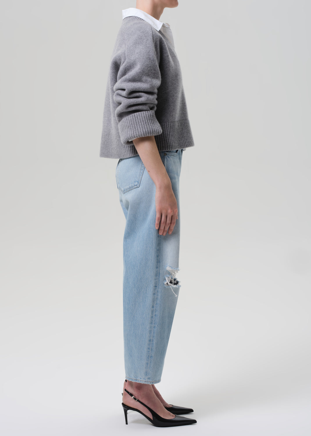 Person wearing a gray sweater and light blue jeans on a plain background