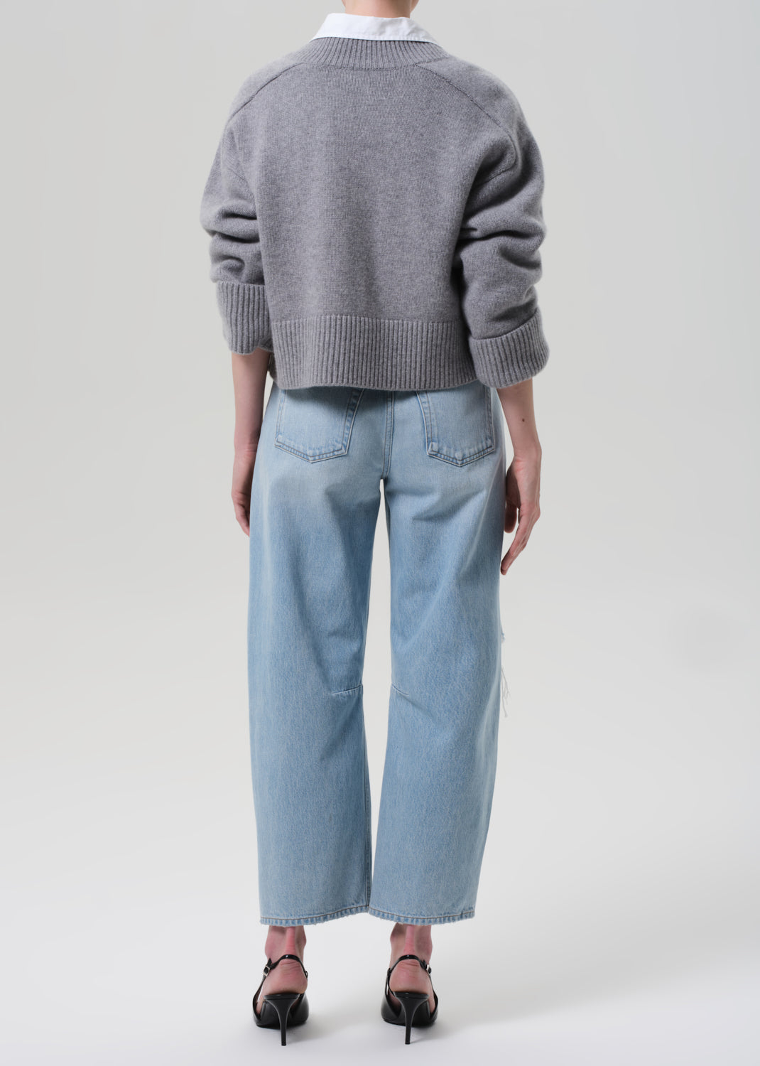 Person wearing a gray sweater and light blue jeans on a white background