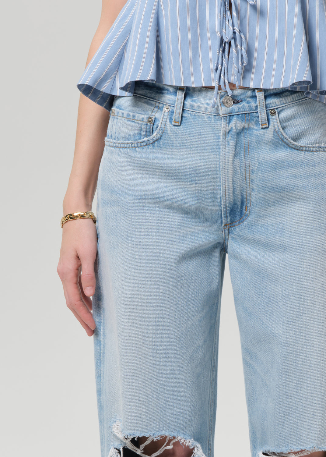 Person wearing a blue striped top and ripped jeans on a plain background