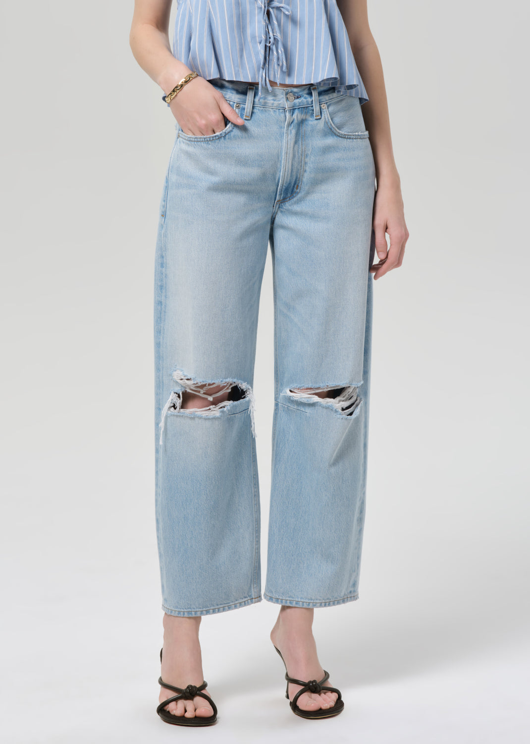 Person wearing a blue striped top and ripped jeans on a plain background