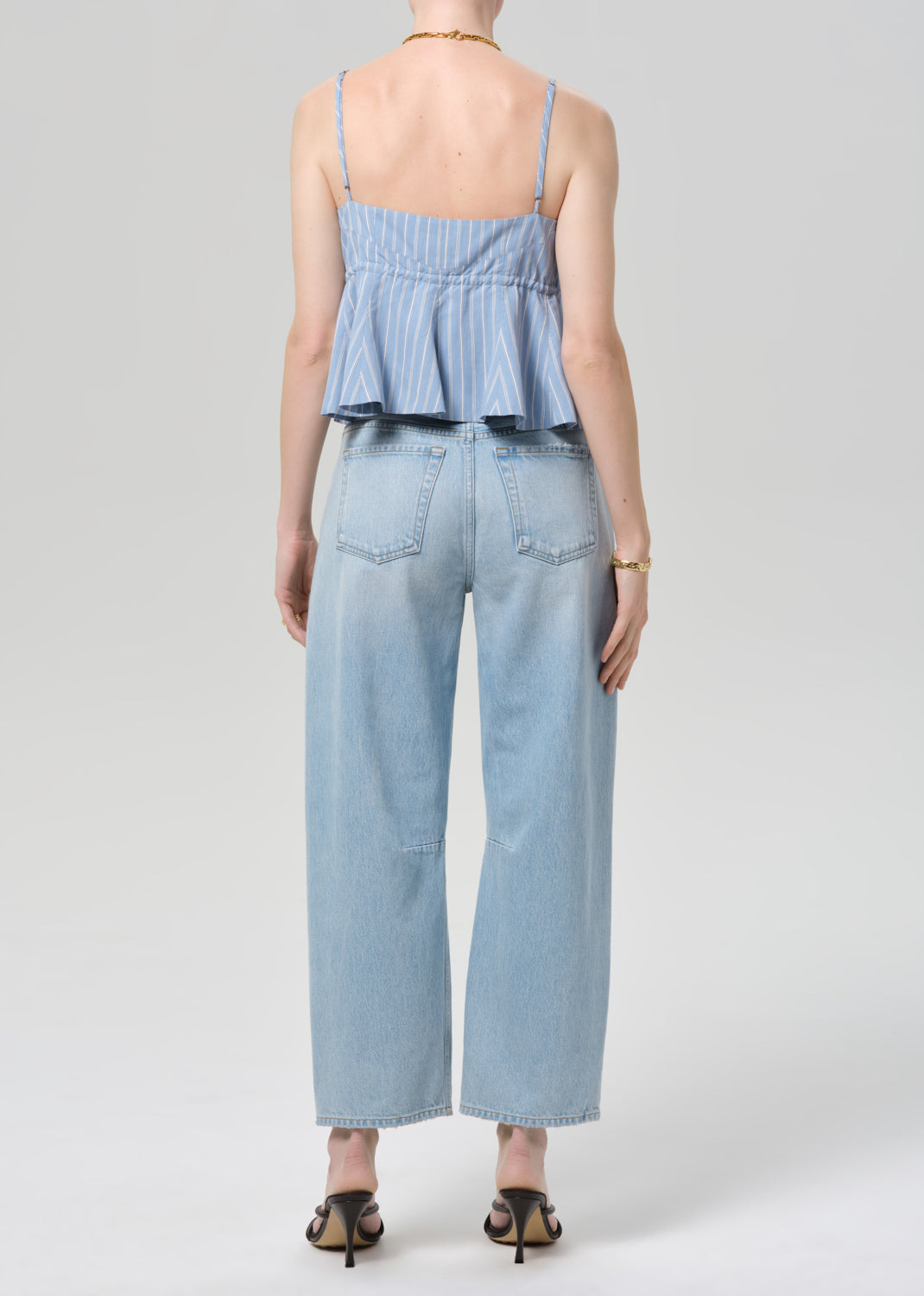 Person wearing a blue striped top and ripped jeans on a plain background