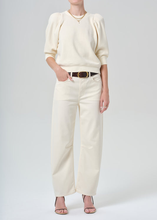 Person wearing a cream sweater and cream pants on a plain background