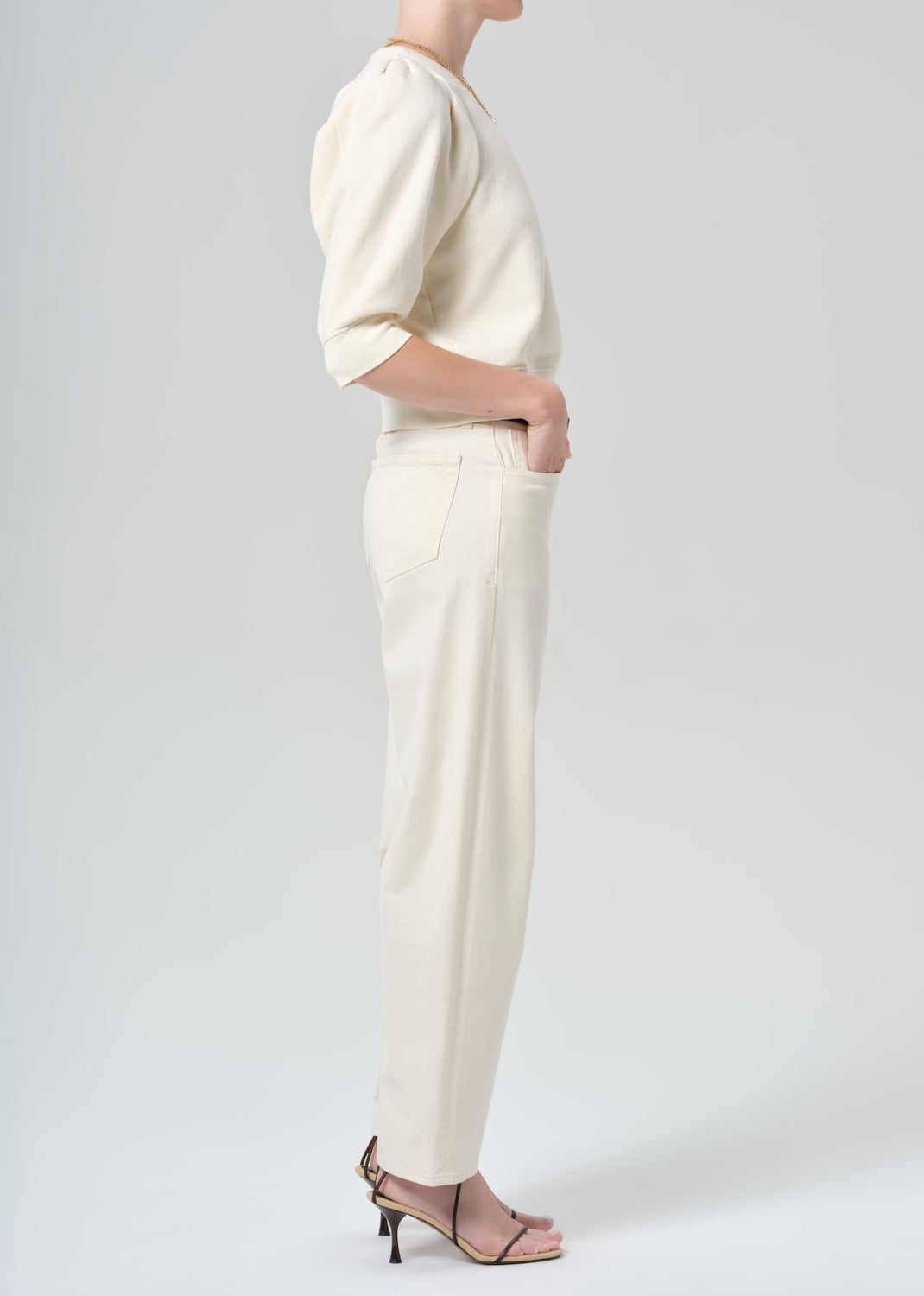 Person wearing a cream sweater and cream pants on a plain background