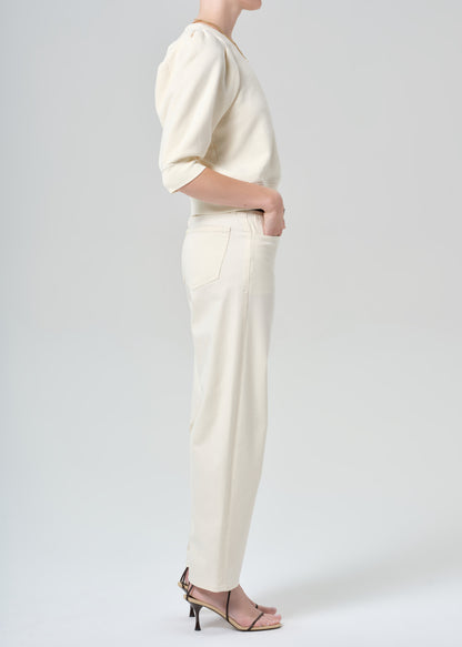 Person wearing a cream sweater and cream pants on a plain background