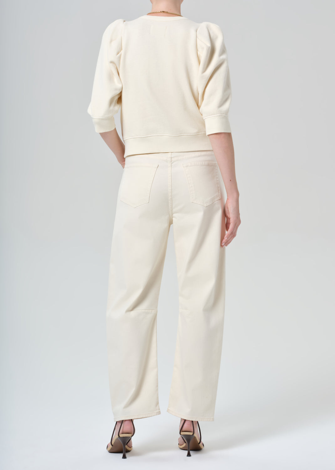 Person wearing a cream sweater and cream pants on a plain background